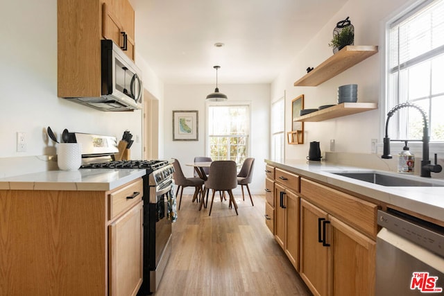 kitchen with appliances with stainless steel finishes, light hardwood / wood-style floors, decorative light fixtures, sink, and plenty of natural light