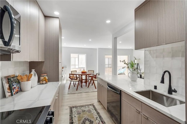 kitchen featuring appliances with stainless steel finishes, light wood-type flooring, backsplash, light stone counters, and sink