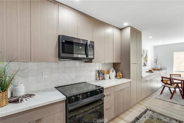 kitchen featuring decorative backsplash, light brown cabinetry, light stone countertops, light hardwood / wood-style flooring, and black electric range oven