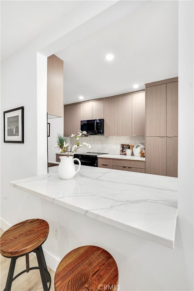 kitchen featuring backsplash, black appliances, light hardwood / wood-style floors, light stone counters, and kitchen peninsula