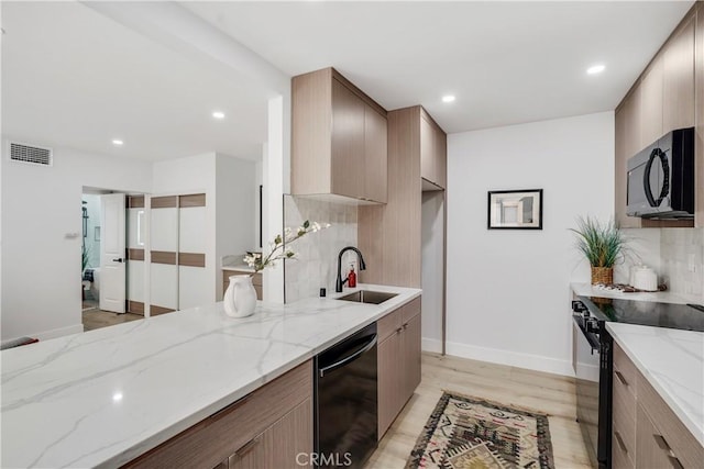 kitchen with black appliances, decorative backsplash, light stone counters, and sink