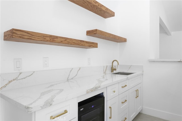 kitchen with light stone countertops, beverage cooler, sink, and white cabinets