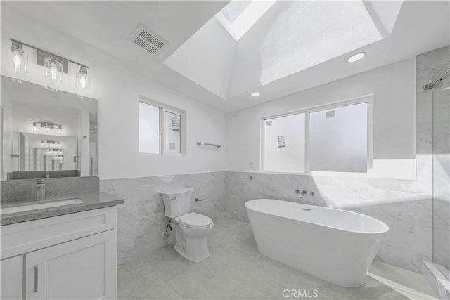 full bathroom with tile walls, vanity, independent shower and bath, a skylight, and toilet