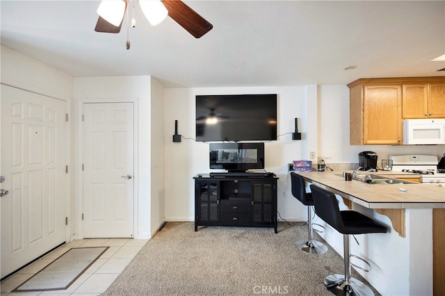 kitchen with white appliances, a breakfast bar area, light tile patterned floors, tile countertops, and ceiling fan