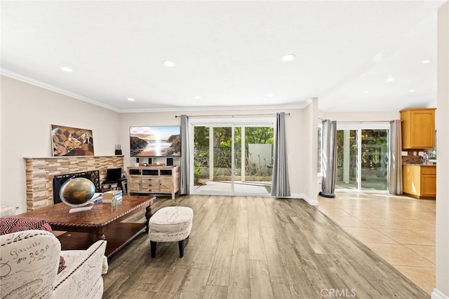 living room with a stone fireplace, crown molding, a wealth of natural light, and light hardwood / wood-style flooring