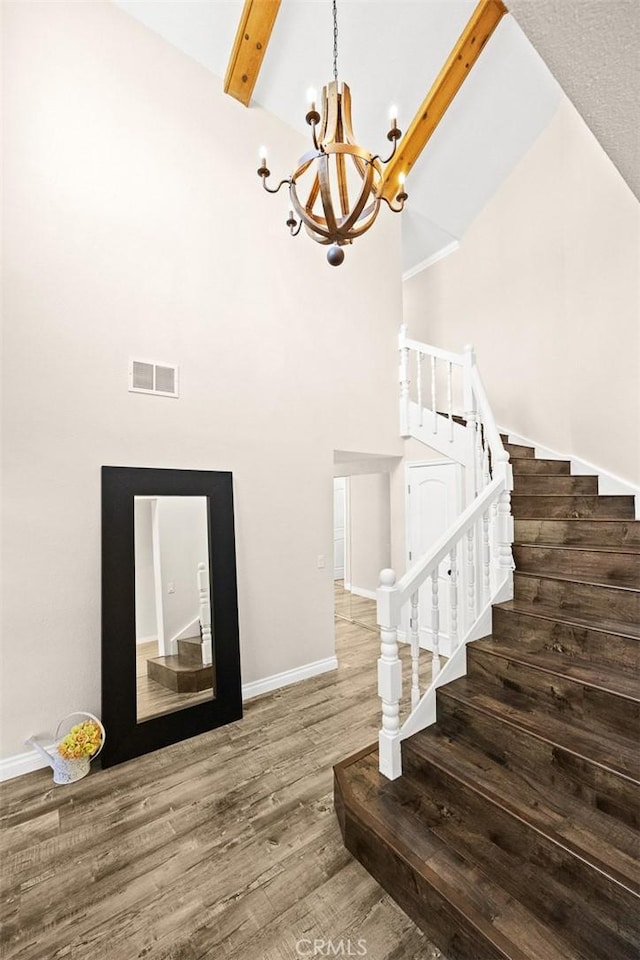 stairway featuring hardwood / wood-style floors, beamed ceiling, high vaulted ceiling, and an inviting chandelier