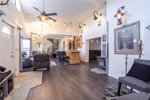 living room with ceiling fan with notable chandelier, dark wood-type flooring, a wood stove, and high vaulted ceiling