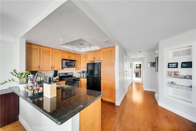 kitchen with kitchen peninsula, a textured ceiling, light hardwood / wood-style flooring, appliances with stainless steel finishes, and dark stone countertops