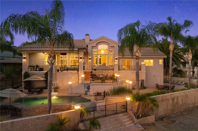 back house at dusk featuring a fenced in pool, a patio area, and a balcony