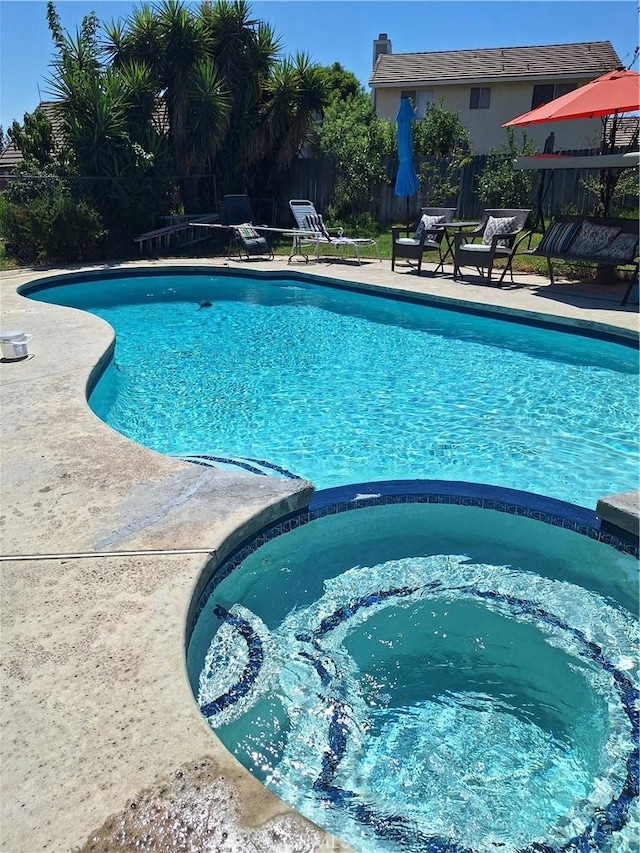 view of pool featuring a patio area, a pool with connected hot tub, and fence