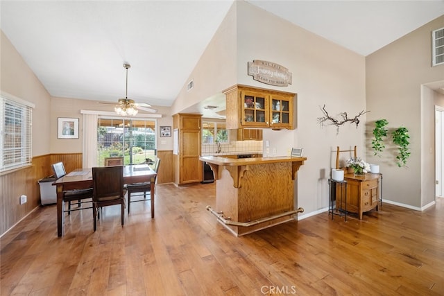 interior space with light wood-type flooring, wood walls, ceiling fan, and high vaulted ceiling