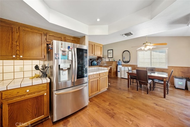 kitchen featuring ceiling fan, light hardwood / wood-style floors, stainless steel fridge, tile countertops, and vaulted ceiling