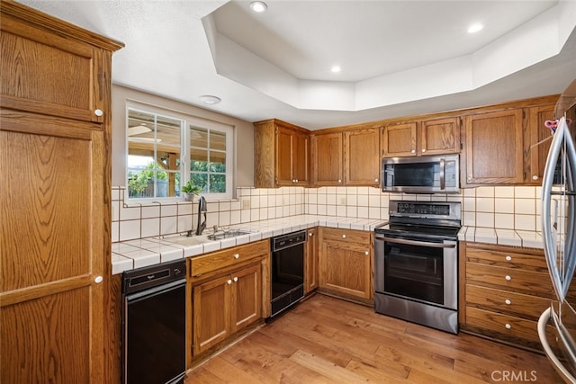 kitchen with a tray ceiling, light hardwood / wood-style flooring, stainless steel appliances, and tile countertops