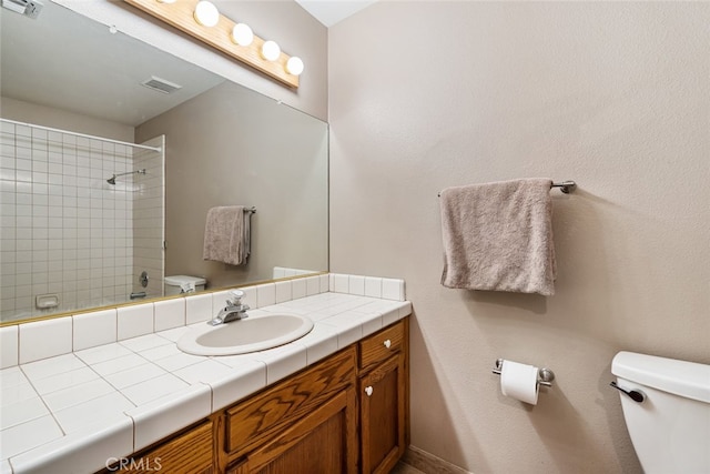 bathroom with a tile shower, vanity, and toilet