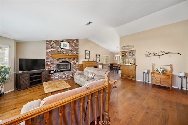 living room with vaulted ceiling, a brick fireplace, and hardwood / wood-style flooring