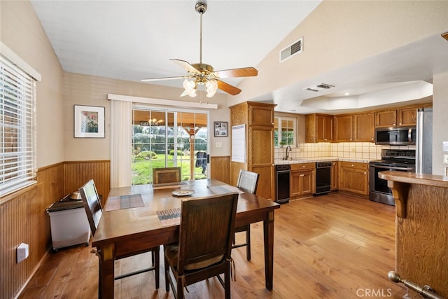 dining space featuring vaulted ceiling, wood walls, light wood-type flooring, ceiling fan, and sink