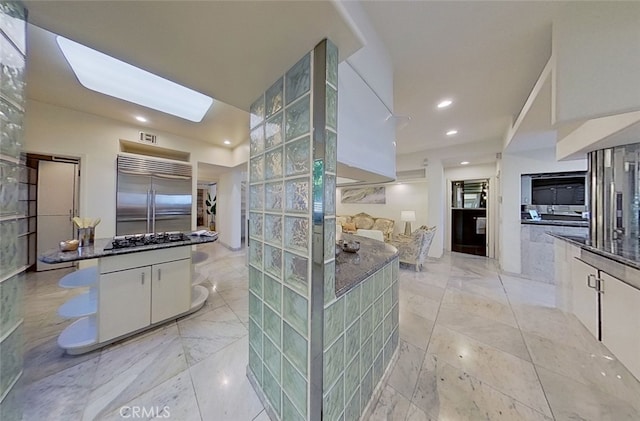 kitchen with white cabinetry, a skylight, stainless steel appliances, and dark stone counters