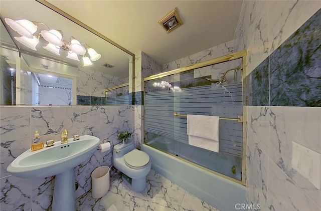 bathroom featuring toilet, shower / bath combination with glass door, and tile walls