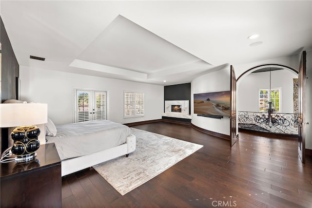 bedroom with a raised ceiling, french doors, dark wood-type flooring, and a notable chandelier