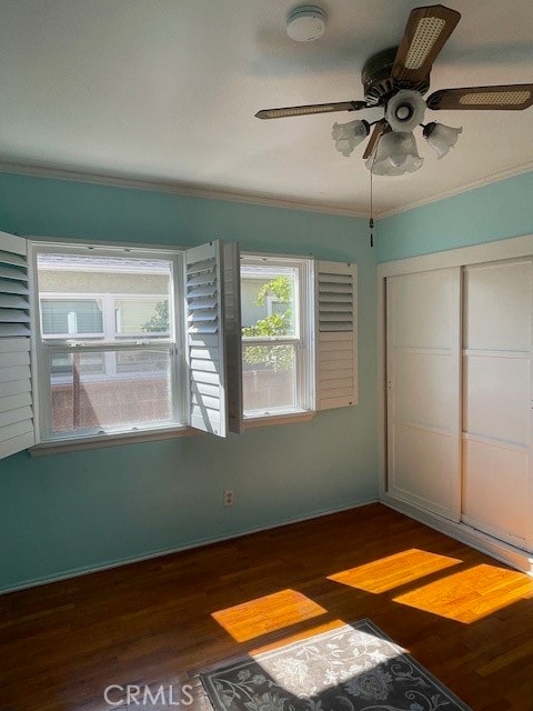 unfurnished bedroom featuring ceiling fan, a closet, dark hardwood / wood-style floors, and crown molding