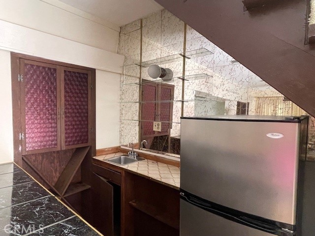 kitchen featuring tile walls, tile countertops, sink, and stainless steel refrigerator