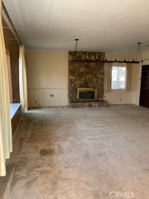 unfurnished living room featuring carpet, crown molding, and a stone fireplace