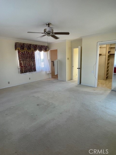 interior space with a closet, light carpet, a walk in closet, ornamental molding, and ceiling fan