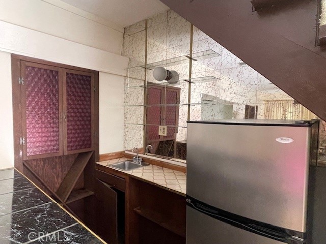 kitchen with tile walls, tile countertops, sink, and stainless steel fridge