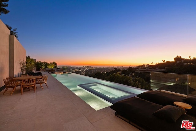 pool at dusk with an in ground hot tub and a patio