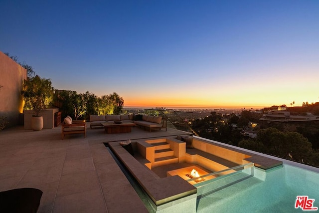 pool at dusk with a patio and an outdoor living space with a fire pit