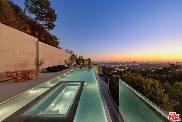 pool at dusk featuring an in ground hot tub and a patio area