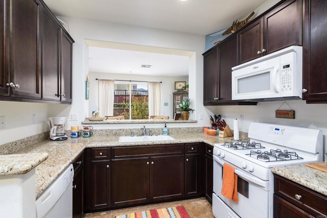 kitchen with dark brown cabinetry, light stone countertops, sink, and white appliances