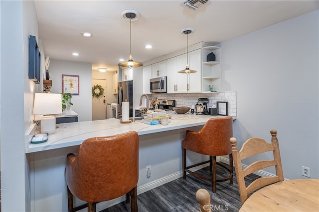 kitchen with light stone counters, backsplash, kitchen peninsula, a breakfast bar area, and stainless steel appliances