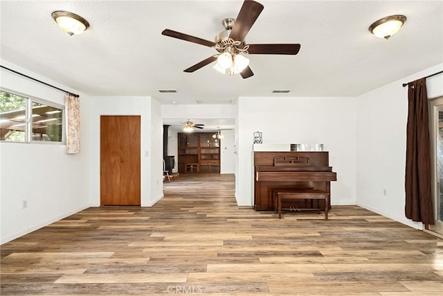 living room featuring light wood-style flooring, visible vents, ceiling fan, and baseboards