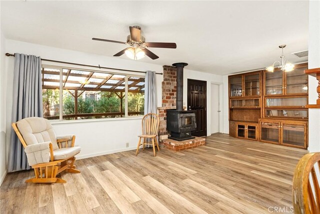interior space with baseboards, light wood-style flooring, a wood stove, visible vents, and ceiling fan with notable chandelier