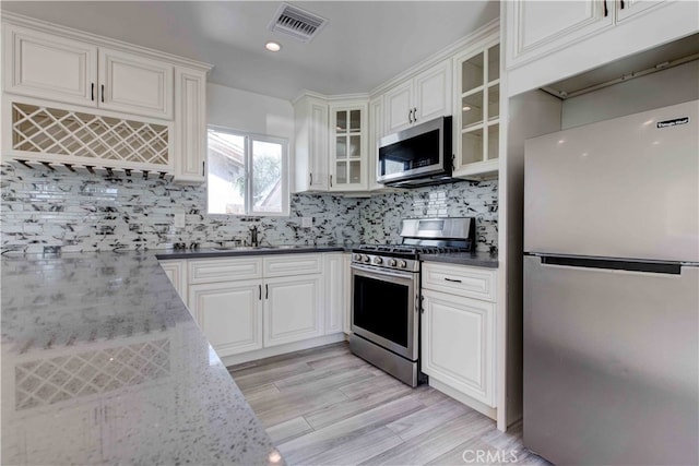 kitchen featuring white cabinetry, backsplash, stainless steel appliances, light hardwood / wood-style flooring, and dark stone counters