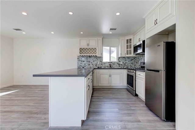 kitchen with light hardwood / wood-style floors, white cabinets, kitchen peninsula, stainless steel appliances, and backsplash