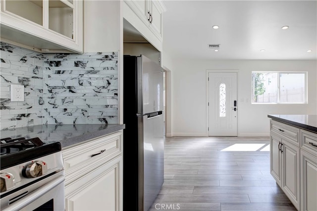 kitchen featuring white cabinetry, stainless steel refrigerator, light hardwood / wood-style flooring, backsplash, and white gas range