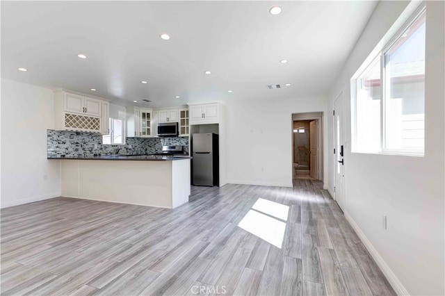 kitchen with appliances with stainless steel finishes, kitchen peninsula, white cabinetry, and light hardwood / wood-style flooring