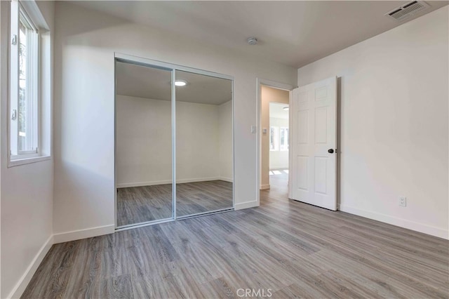 unfurnished bedroom with multiple windows, wood-type flooring, and a closet