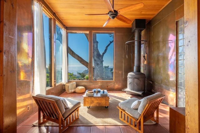 sunroom / solarium with ceiling fan, a wood stove, and wood ceiling