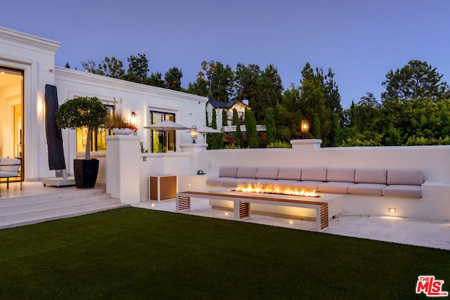 back house at dusk with a patio, a yard, a wooden deck, and a fire pit