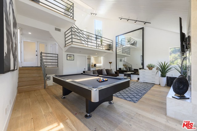 rec room featuring light wood-type flooring, a healthy amount of sunlight, and a towering ceiling