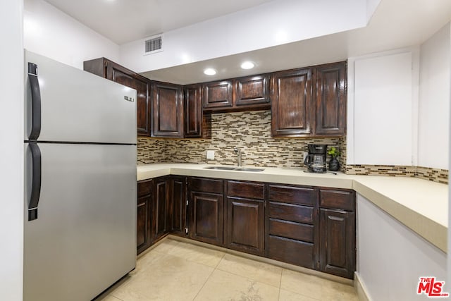 kitchen with dark brown cabinetry, stainless steel fridge, light tile patterned floors, sink, and decorative backsplash