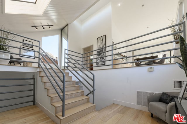 staircase with rail lighting, a high ceiling, hardwood / wood-style floors, and a skylight