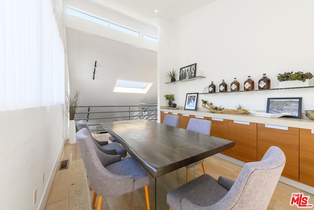 dining room featuring a high ceiling, light hardwood / wood-style floors, and a skylight