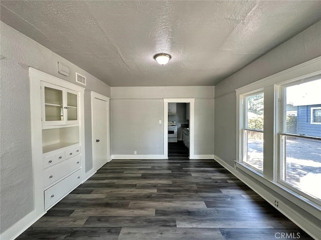 unfurnished room featuring a textured ceiling, dark wood-type flooring, and built in features