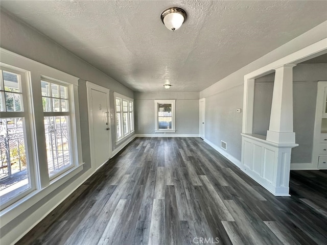 unfurnished living room featuring a textured ceiling, dark hardwood / wood-style floors, and ornate columns