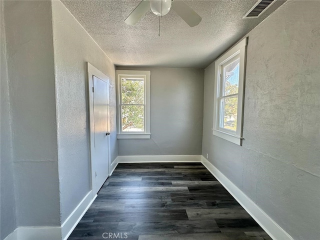 empty room featuring a wealth of natural light, a textured ceiling, ceiling fan, and dark hardwood / wood-style flooring