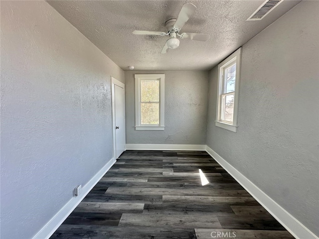 empty room featuring a textured ceiling, a healthy amount of sunlight, dark hardwood / wood-style flooring, and ceiling fan